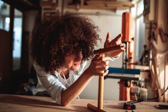 Young craftswoman aligning wooden dowel in home workshop