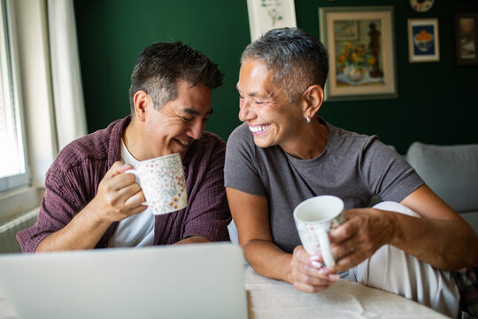 Smiling couple drinking coffee at home with laptop