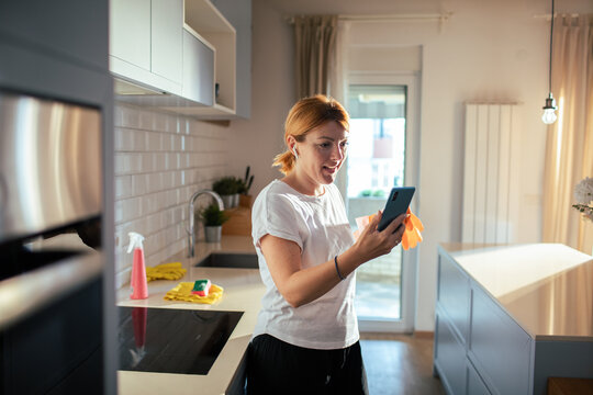 Woman using smartphone while cleaning kitchen at home