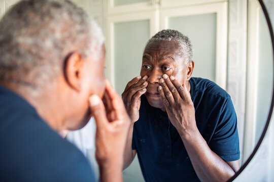 Senior man checking face in bathroom mirror at home