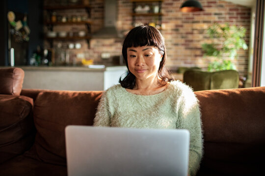 Smiling woman using laptop on home sofa