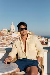 Naklejka premium Man in sunglasses drinking espresso on terrace with coastal city skyline for summer travel lifestyle background and cool leisure portrait