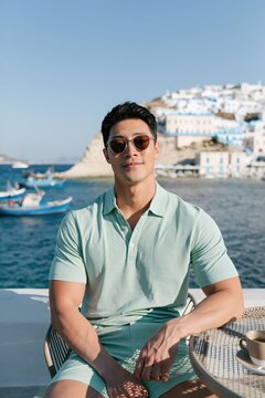 Young man in a mint polo and sunglasses at a mediterranean harbor with boats for travel background and lifestyle portrait
