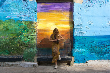 Mature woman searching through her crossbody bag while leaning against a colorful mural wall in Cartagena. Travel essentials and trip preparation concept. © Gonzalo