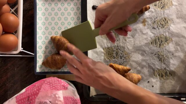 Manos sacando croissants del horno con paleta desde cenital
