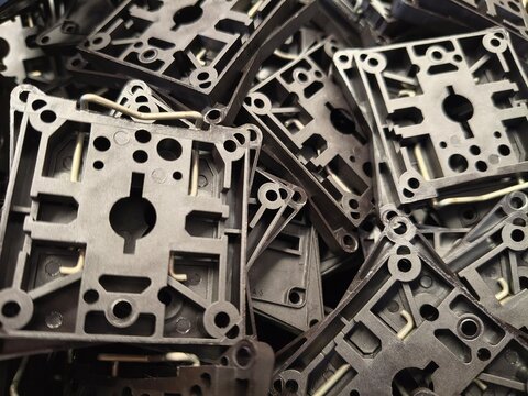 Pile of black plastic technical mounting components with metal springs, industrial spare parts texture background