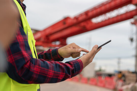 Construction worker using smartphone at construction site, with blurred steel structure in background. Concept of construction technology,