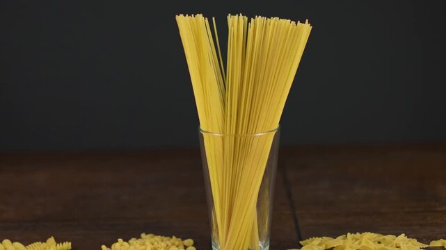 Uncooked spaghetti bundle standing upright in clear glass on dark wooden table with black background, with spaghetti, pasta, uncooked, dry detail, showing glass, bundle, vertical, strand context