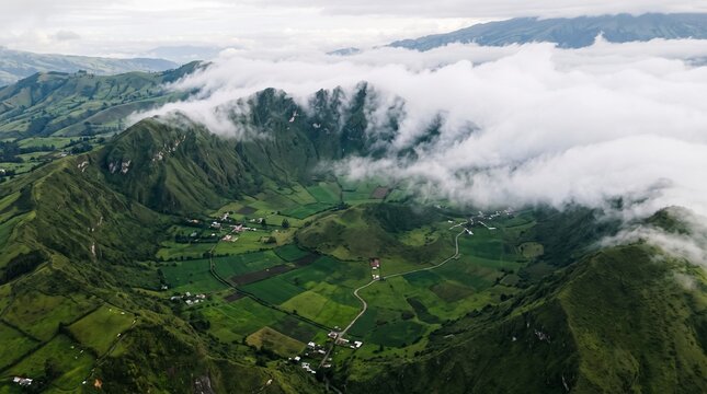 Pululahua volcanic crater with white clouds rolling over steep mountain ridges into the green valley aerial wide shot for travel editorial marketing
