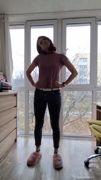 Young person stands in room with big windows while wearing casual clothes and slippers