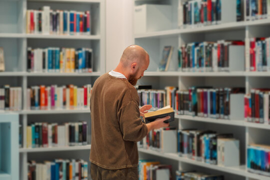 Rear view of a man reading between library shelves