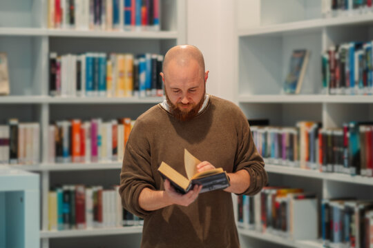 Man reading an open book in front of library shelves