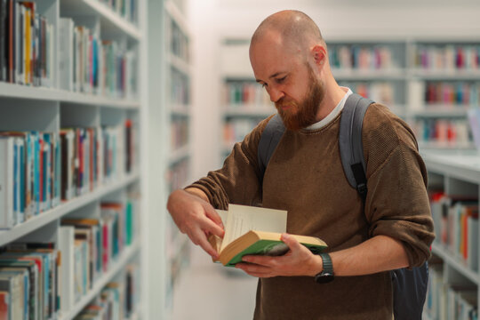 Man opening a book he has taken from a library shelf