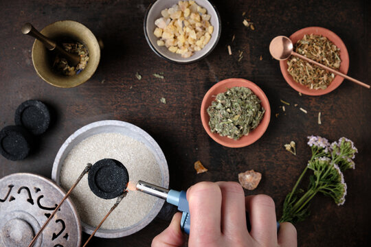 Incense ritual preparation with frankincense and dried herbs - lighting the charcoal