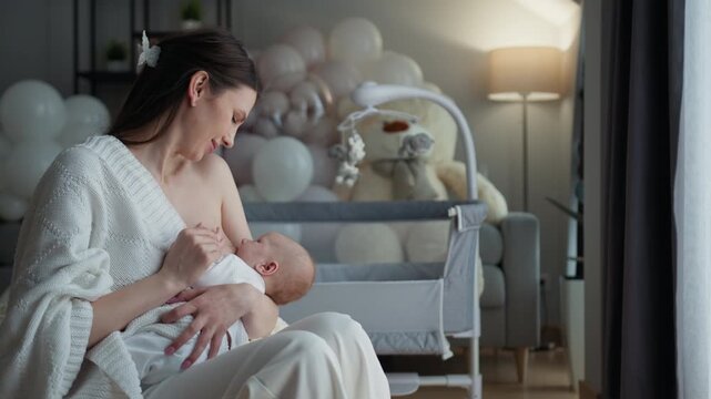 Mother lovingly breastfeeds infant child in cozy nursery with balloons and soft toys. Woman parent child family love parenthood maternity home adorable moment childhood innocence peaceful calm