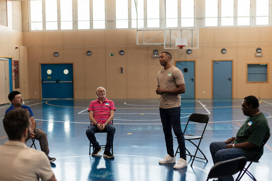 Community leader speaking to diverse group of men in gymnasium