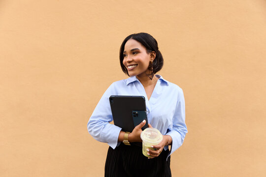 Happy hispanic woman holding tablet standing in front of orange wall