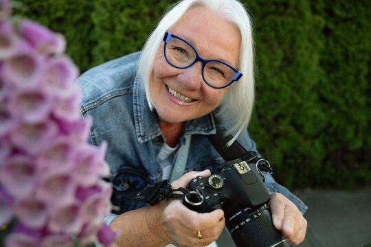 Smiling senior woman photographer with camera in garden