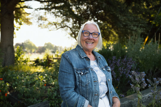Smiling senior woman in denim jacket enjoying a sunny garden