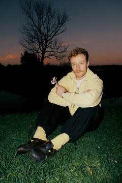 Man sitting on grass at sunset with tree in background