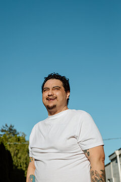 Candid portrait of a smiling man with tattoos under blue sky