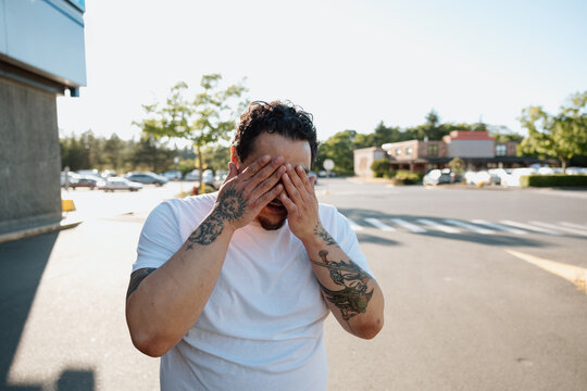 Candid tattooed man covering his face in a sunny parking lot