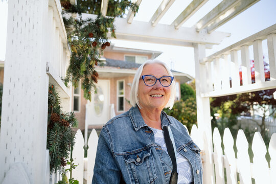 Smiling senior woman at white picket gate with plants growing above