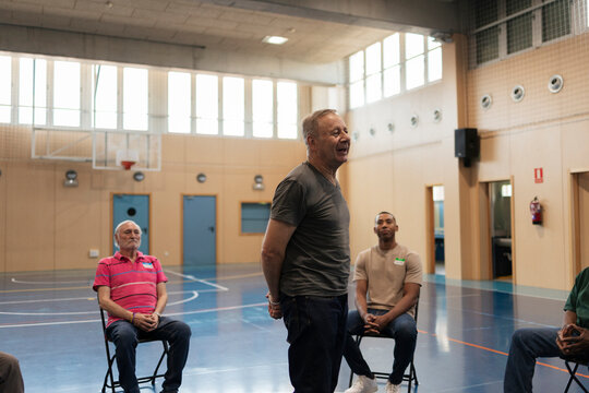 Senior man speaking to diverse group in gymnasium