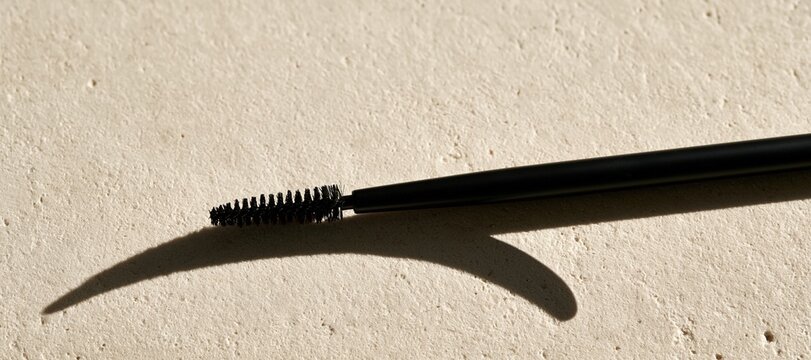 Brow brush casting abstract eyebrow - shaped shadow on pale textured stone