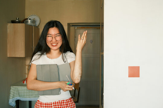 Happy young asian female student holding a tablet and planning at home