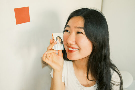Young happy asian woman holding a small instant photo of herself 