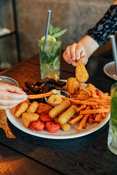 Two diners share a large platter of fries and assorted fried snacks with dipping sauce, accompanied by refreshing mint and lime drinks at a restaurant table