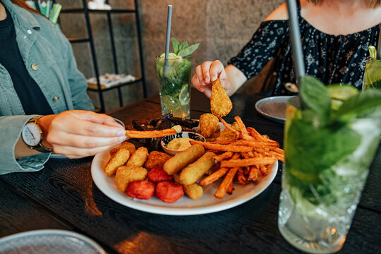 Two diners share a large platter of fries and assorted fried snacks with dipping sauce, accompanied by refreshing mint and lime drinks at a restaurant table