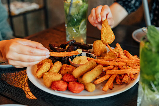 Two diners share a large platter of fries and assorted fried snacks with dipping sauce, accompanied by refreshing mint and lime drinks at a restaurant table