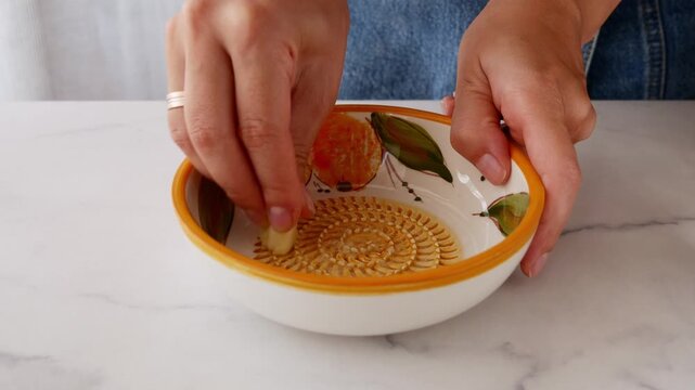 Close-up of hands grating fresh garlic on traditional Spanish ceramic grater plate. Authentic Mediterranean food preparation using special plato rallador.