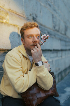 Man sits against a wall holding a flower in a city setting