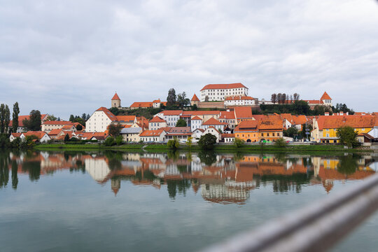 Ptuj, Slovenia shows its historic buildings beside the Drava River. Ptuj Castle stands above the town under cloudy skies.