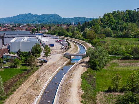 Aerial view shows channel cleaning and widening work for flood prevention near a town. Raised embankments support river management.