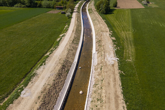Aerial view of river channel restoration in a rural area showing widened waterway and embankments. Focus on flood prevention techniques.