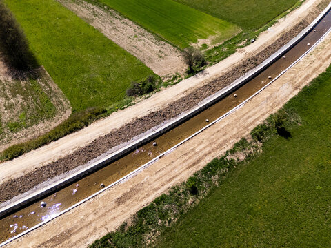 A drone view shows a river restoration site where channel cleaning, widening, and raised embankment construction are in progress.