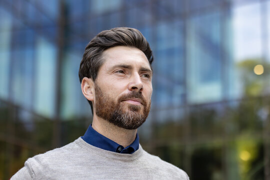 Close-up photo of a young male businessman, profile on the left, standing looking forward near an office building