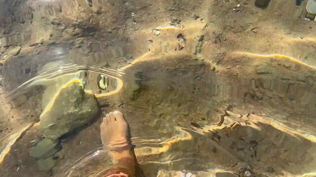 Inquadratura in soggettiva dei piedi di una donna che cammina su un fondale sabbioso in un mare limpido e poco profondo