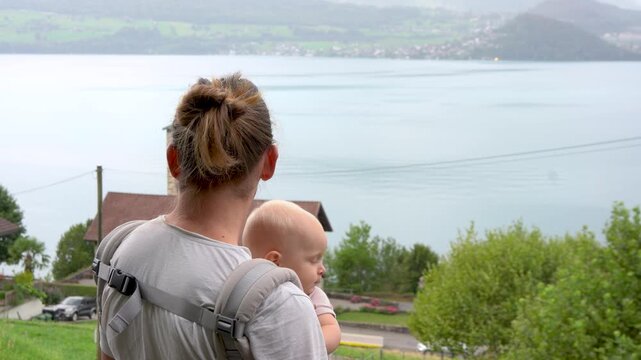 Father carries baby on back, gazing at lake Thun Switzerland
