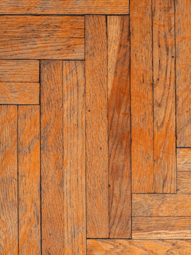 Old worn wooden parquet floor with geometric herringbone pattern and visible scratches.