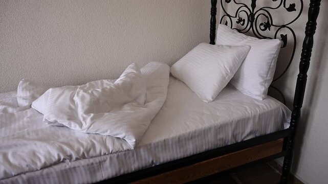 Unmade single bed with crumpled white linen in bedroom for hotel room cleaning, morning routine house chore and insomnia sleep disorder concept, morning wake up routine, room housekeeping