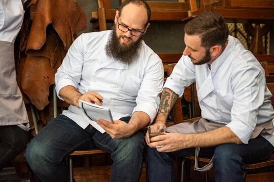 Two male chefs discussing something on a tablet in a kitchen setting.