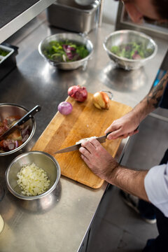 Person chopping onions on a wooden board in a professional kitchen.