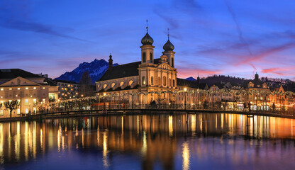 Naklejka premium Splended sunset over the Jesuit church with Pilatus mountain at background in the evening and Rathaussteg in Christmas illumination, Switzerland