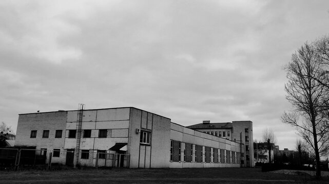 Black and white view of a minimalist industrial brick building and warehouse under a dramatic cloudy sky