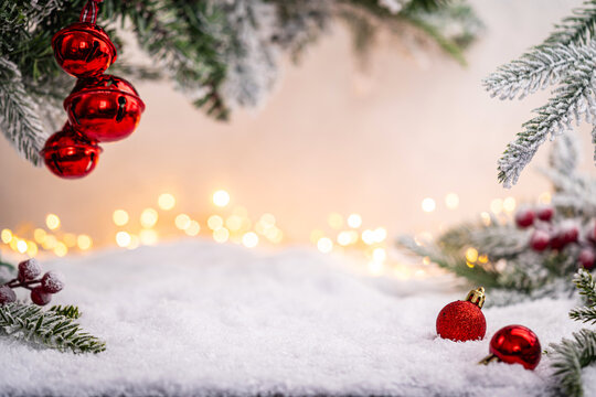 Festive red baubles rest on snow beneath frosted pine branches and golden holiday lights in the background. Winter Christmas Holiday Decoration Background